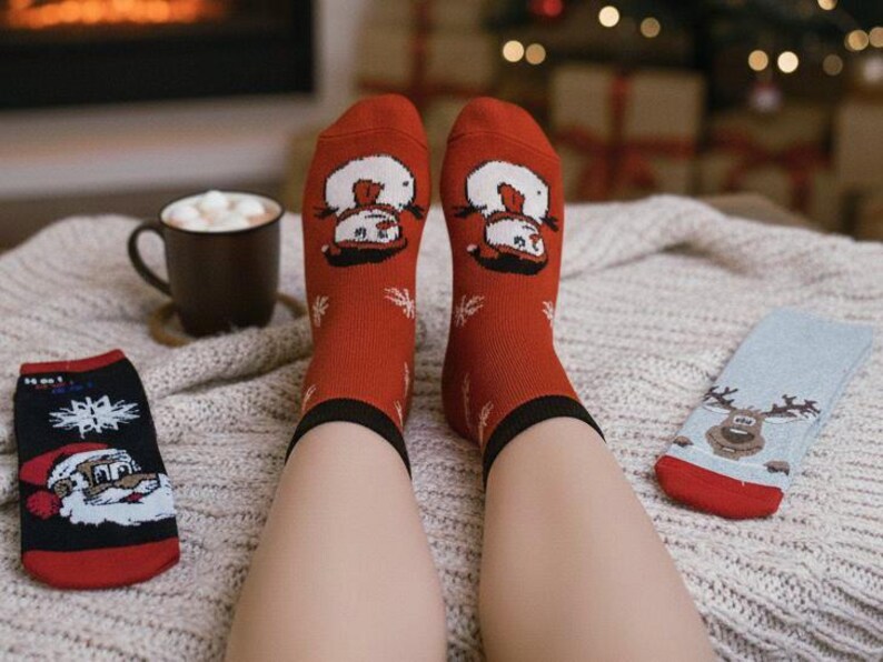 Cozy winter scene with christmas festive socks featuring snowmen, Santa, and a reindeer, alongside a hot chocolate in a mug by a warm fireplace.