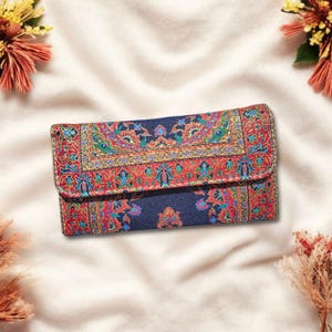 May include: A rectangular, patterned clutch with a fold-over flap. The clutch features a navy blue background with a detailed, colorful design in red, green, yellow, and blue. The design has an ornate, floral pattern.