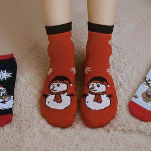 Cozy winter scene with christmas festive socks featuring snowmen on womans feet, Santa, and a reindeer patterns laying next to it on the carpet.
