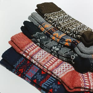 May include: A stack of five pairs of colorful patterned socks. The socks are made of a soft, knitted fabric and feature a variety of geometric and floral designs. The socks are a mix of red, blue, black, brown, and white.