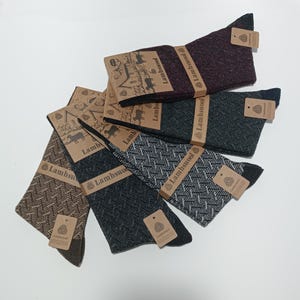 Peut inclure: Cinq paires de chaussettes avec des motifs différents. Les chaussettes sont en laine d'agneau et portent une étiquette brune avec le mot "Lambswool" dessus.