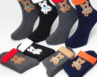 May include: A collection of cozy socks in various colors, including gray, black, and navy blue. Each sock features a teddy bear design with a blue bow and a contrasting cuff. The socks are displayed on white mannequin legs.
