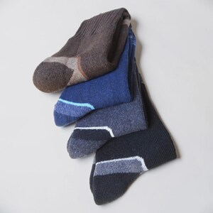 May include: A set of four crew socks stacked vertically, featuring a ribbed cuff and a reinforced heel and toe area. The colors include brown, royal blue, heather gray, and black, each with a distinct contrasting color accent at the toe.