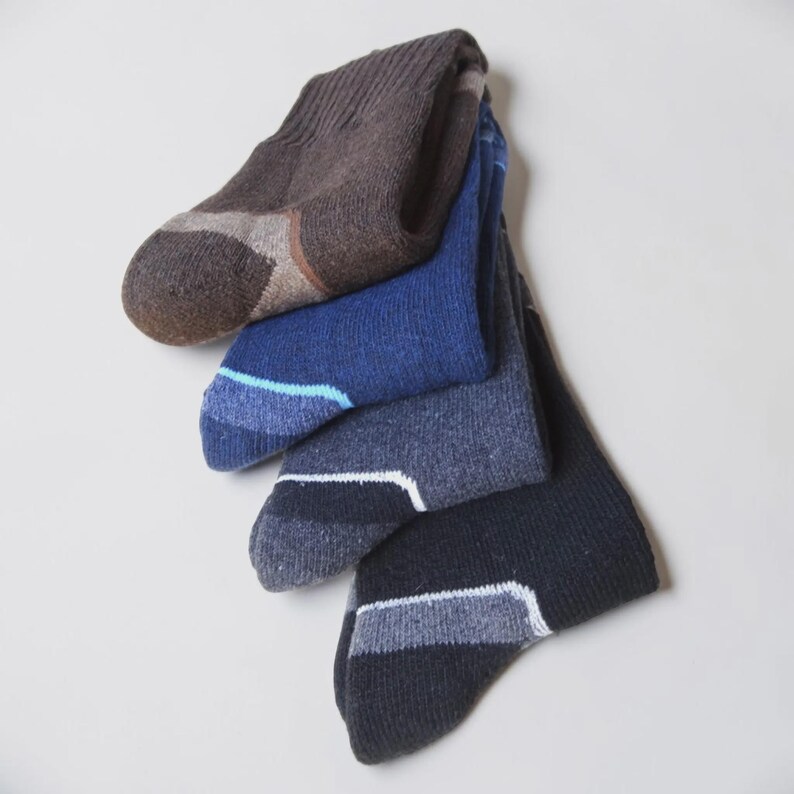 May include: A set of four crew socks stacked vertically, featuring a ribbed cuff and a reinforced heel and toe area. The colors include brown, royal blue, heather gray, and black, each with a distinct contrasting color accent at the toe.
