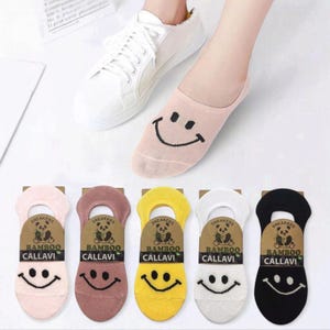 A foot in a white sneaker wearing a pink smiley face sock, with colorful socks displayed beneath: pink, brown, yellow, white, and black.