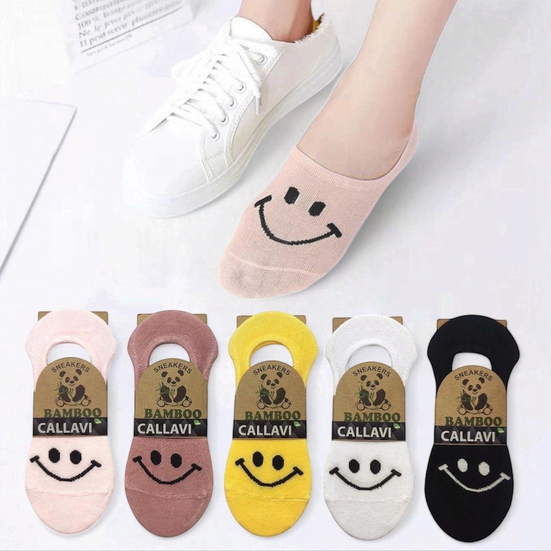 A foot in a white sneaker wearing a pink smiley face sock, with colorful socks displayed beneath: pink, brown, yellow, white, and black.
