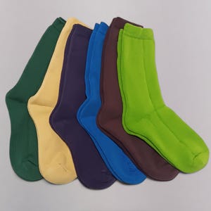 Five colorful socks in green, dark green, beige, purple, blue, and brown, displayed overlapping each other on a light gray surface.