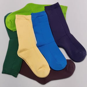 A colorful selection of cotton socks in grass green, dark green, beige, blue, dark maroon color, and purple laid out on a neutral background, showcasing a vibrant assortment for fashion and comfort enthusiasts.
