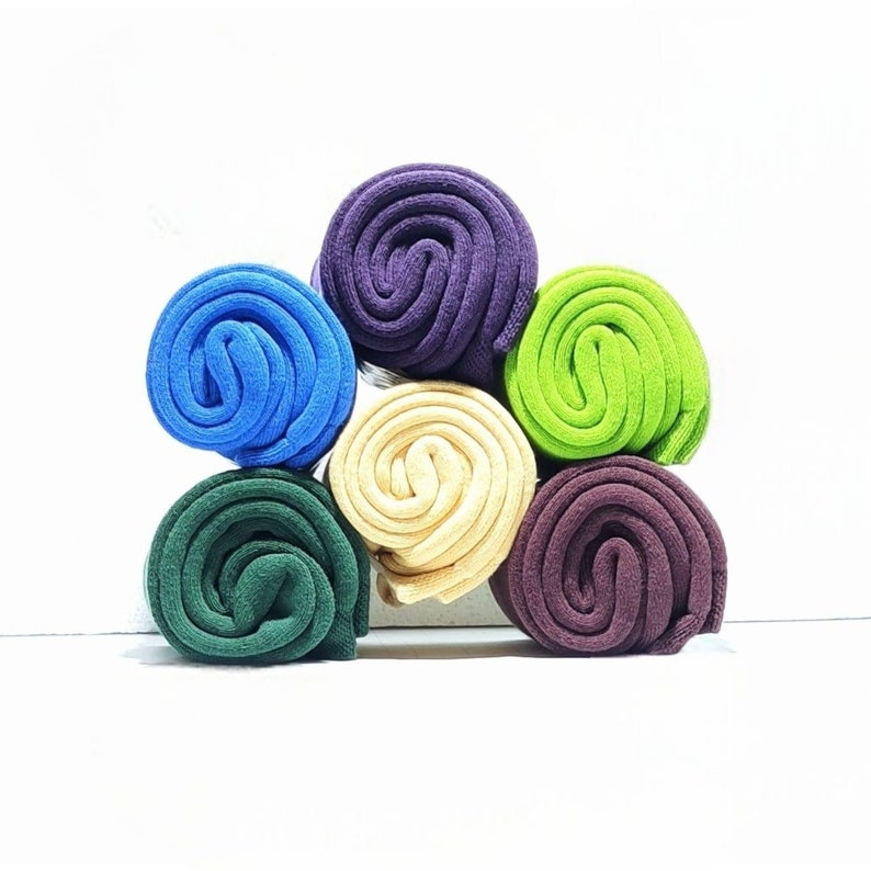 Six pairs of socks rolls  in various color are displayed on a white background, on top of each other. Their colors are: Burgundy, Blue, Green, Light green, light brown, Purple