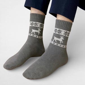 Gray alpaca socks featuring white reindeer and snowflake patterns are worn with navy pants. The cozy and festive design conveys a warm, wintry feel.