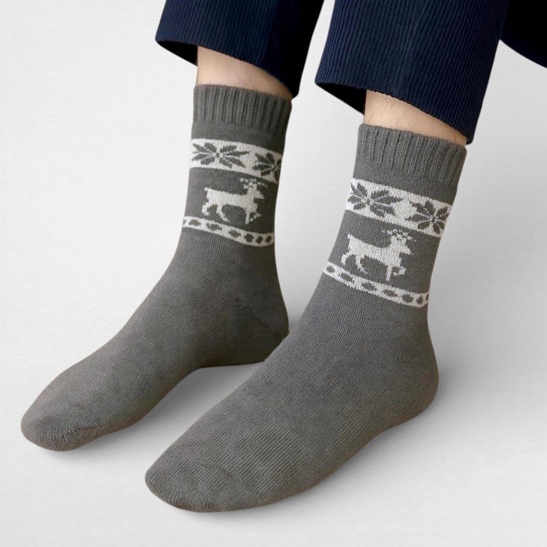 Gray alpaca socks featuring white reindeer and snowflake patterns are worn with navy pants. The cozy and festive design conveys a warm, wintry feel.