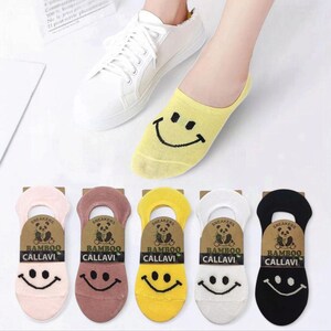 A foot wearing a yellow smiley face sock next to a white sneaker, with colorful socks featured below, showcasing playful designs.
