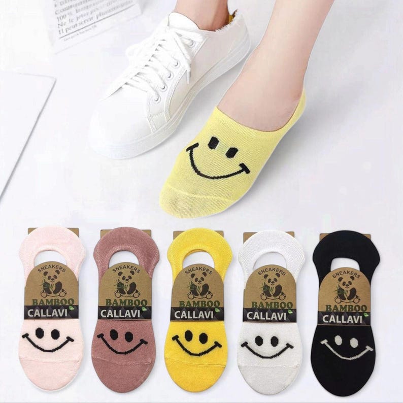 A foot wearing a yellow smiley face sock next to a white sneaker, with colorful socks featured below, showcasing playful designs.