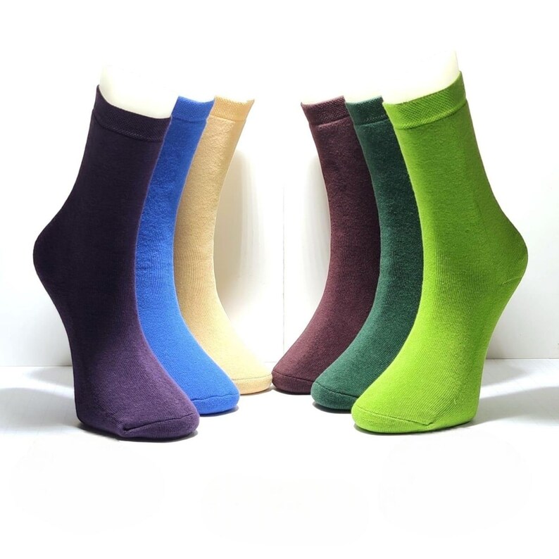 Six pairs of socks in various color are displayed on a white background, on foot mannequins. Their colors are: Burgundy, Blue, Green, Light green, light brown, Purple