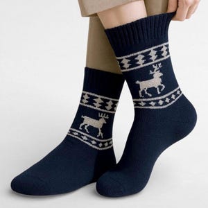 Navy blue alpaca socks featuring white reindeer and snowflake patterns are worn with beige pants. The cozy and festive design conveys a warm, wintry feel. The quarter cut is visible.