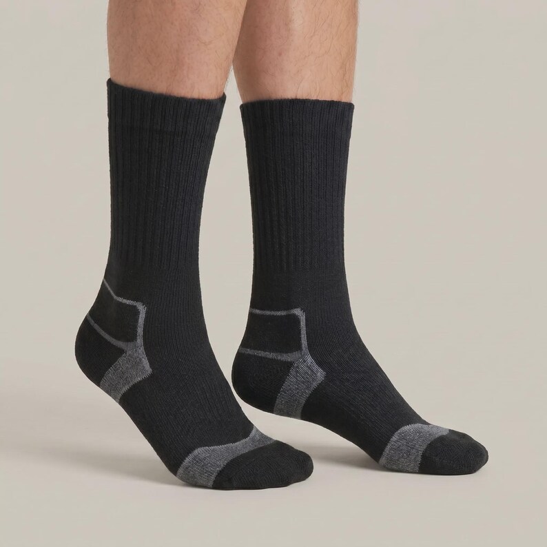 May include: A pair of black crew-length socks featuring a ribbed texture on the leg. The socks include contrasting dark gray reinforced panels at the heel and toe areas, providing a distinct visual detail against the solid black fabric base.
