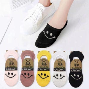 A foot wearing a black smiley face sock next to white sneakers, with colorful bamboo socks featuring smiley faces displayed below.