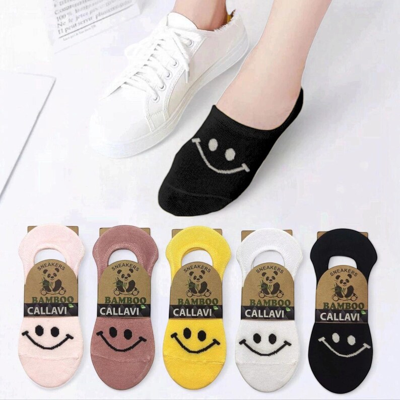 A foot wearing a black smiley face sock next to white sneakers, with colorful bamboo socks featuring smiley faces displayed below.