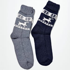 Two alpaca socks are laid out side by side. One gray, the other navy, both featuring white reindeer and snowflake patterns, evoking a cozy winter festive vibe.