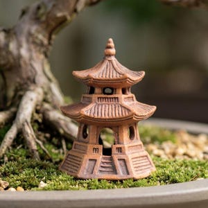 May include: A miniature terracotta-colored pagoda ornament featuring a multi-tiered roof structure with detailed eaves and open arched doorways, designed with a hexagonal base and textured surfaces, positioned as a decorative garden accent.