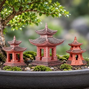 Op de afbeelding: Drie miniatuur pagodestructuren in terracotta-kleur met donkerbruine, getextureerde daken staan in een ondiepe, donkergrijze ronde plantenbak gevuld met donkere aarde, kleine steentjes en stukjes groen mos onder een bonsaiboom.