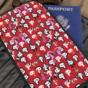 Peut inclure: Un portefeuille de passeport rouge avec une bordure noire et un motif répété de crânes blancs et de personnages de dessins animés. Le portefeuille est ouvert, révélant un passeport bleu.