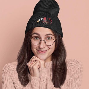 Op de afbeelding: Een zwarte beanie met een kleurrijk geborduurd ontwerp. De beanie wordt gedragen door een persoon die een roze trui en een bril draagt. De afbeelding bevat de tekst "DCOVIBE.ETSY.COM - FIERCE STREETWEAR."