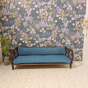 May include: A small teal blue couch with a wooden frame and floral wallpaper in the background.