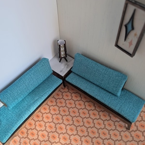 Puede incluir: Dos sofás de tela azul turquesa con marcos de madera se encuentran sobre un suelo estampado. Una mesa pequeña con una lámpara se encuentra entre los sofás.