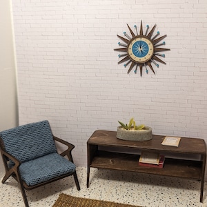 May include: A mid-century modern living room with a blue armchair, a wooden side table with a potted succulent plant and books, and a large starburst clock on the white brick wall.