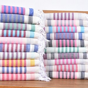 May include: A stack of colourful striped towels with white fringe. The towels are folded and stacked on a wooden surface.