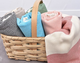 Puede incluir: Una cesta de mimbre llena de toallas turcas de colores. Las toallas están enrolladas y presentan un patrón de diamantes. Las toallas son de color negro, blanco, azul, verde y rosa.