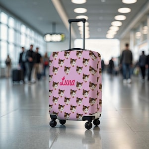 Peut inclure: Une valise à roulettes rose ornée d'un motif répété de têtes de chat. Le mot "Luna" est écrit en rose. La valise est équipée d'une poignée rétractable et de quatre roues noires.