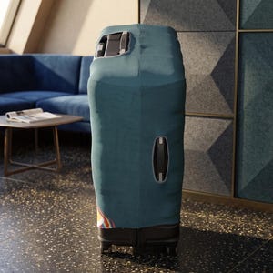 K&ouml;nnte beinhalten: Ein t&uuml;rkisfarbener Koffer mit Schutzh&uuml;lle steht aufrecht. Die H&uuml;lle hat &Ouml;ffnungen f&uuml;r den Griff und einen Seitengriff. Der Koffer steht auf Rollen und befindet sich in einem Raum mit einem blauen Sofa und einem kleinen Tisch.