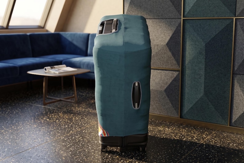 K&ouml;nnte beinhalten: Ein t&uuml;rkisfarbener Koffer mit Schutzh&uuml;lle steht aufrecht. Die H&uuml;lle hat &Ouml;ffnungen f&uuml;r den Griff und einen Seitengriff. Der Koffer steht auf Rollen und befindet sich in einem Raum mit einem blauen Sofa und einem kleinen Tisch.