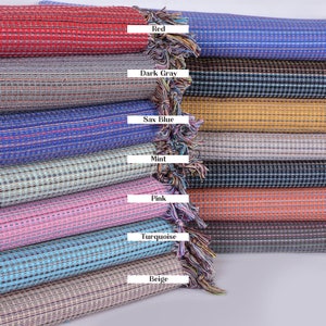 Puede incluir: Una pila de diez toallas turcas tejidas en varios colores, incluyendo rojo, azul petróleo, gris oscuro, negro, azul saxo, mostaza, gris claro, menta, azul marino, rosa, naranja, turquesa, verde caqui y beige. Cada toalla tiene una franja en el extremo.