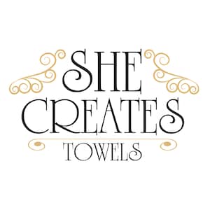 May include: Black and white logo with the text "SHE CREATES TOWELS" in a decorative font. The logo is framed by two gold swirls.