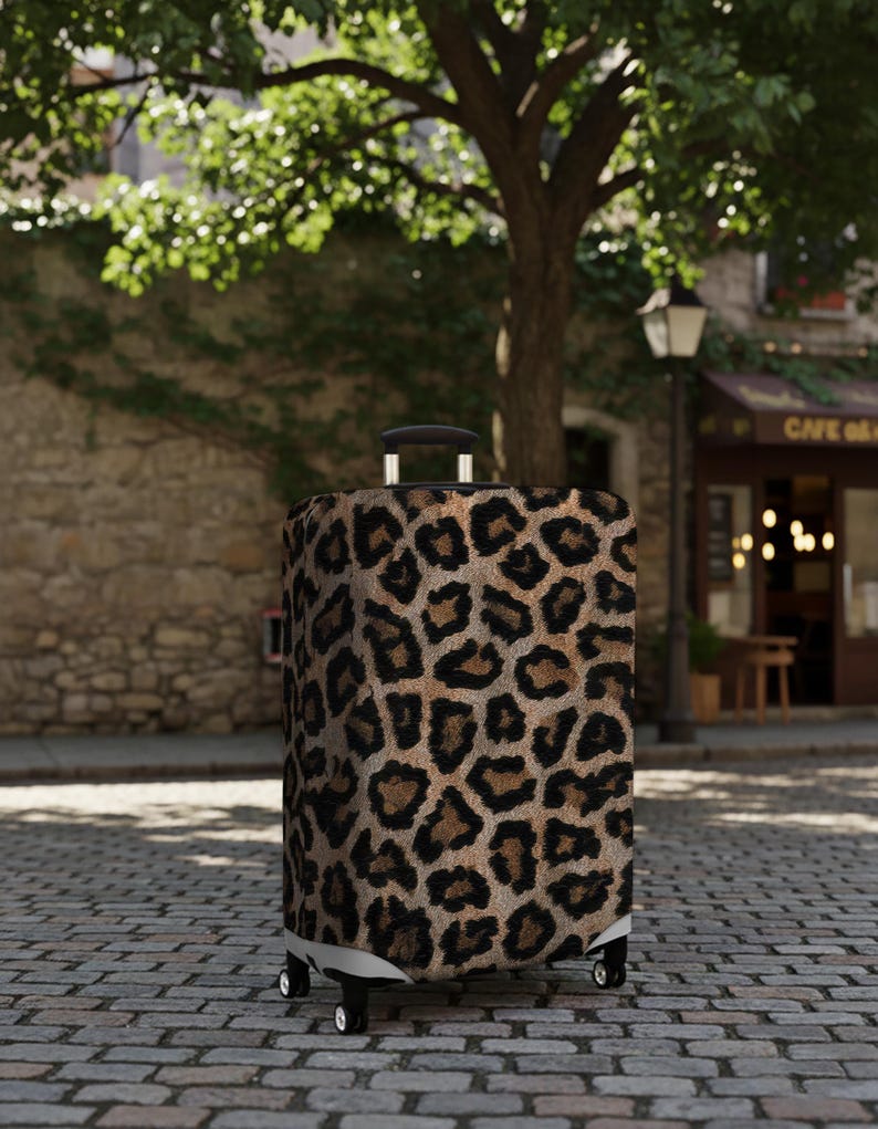 Pode incluir: Uma mala com rodas com um design de estampa de leopardo. A mala tem uma al&ccedil;a e rodas pretas. O fundo mostra uma rua de paralelep&iacute;pedos, uma &aacute;rvore e um edif&iacute;cio com um caf&eacute;.