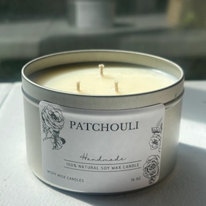 May include: A 16 oz soy wax candle in a round silver metal tin with three wicks. The white label features black text reading PATCHOULI, Handmade, 100% NATURAL SOY WAX CANDLE, WISPY WICK CANDLES, 16 OZ, and illustrations of roses on the sides.