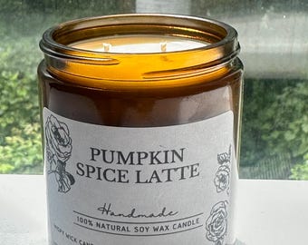 May include: A candle in an amber glass jar with a white label featuring the text PUMPKIN SPICE LATTE, Handmade, 100% NATURAL SOY WAX CANDLE, and WISPY WICK CANDLES, decorated with black line art illustrations of roses on the left and right sides.