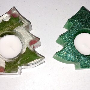 Peut inclure: Deux bougeoirs en forme de sapin de Noël. L'un est transparent avec des paillettes vertes et rouges, l'autre est vert avec des paillettes.