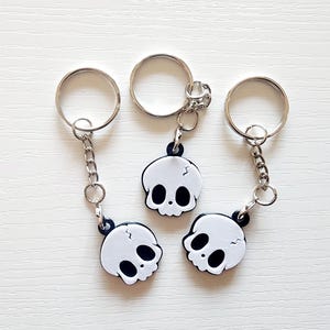 May include: Three silver keychains with white skull charms. Each skull has black eyes and a crack in the top.