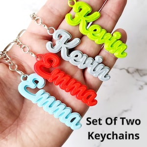 May include: Set of two personalized keychains with the names Emma and Kevin. The keychains are made of plastic and come in a variety of colors, including red, blue, silver, and green.  "Set Of Two Keychains" is written in black text at the bottom of the image.