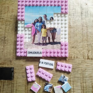May include: A custom photo mosaic constructed from interlocking plastic building blocks. The frame is made of pink and white bricks. The central image shows a family on a beach. A white brick features the text FAMILIENURLAUB, with additional loose bricks and photo tiles labeled B IN PORTUGAL.