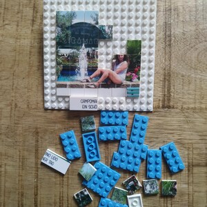 May include: A white plastic building block baseplate featuring a photo mosaic of a fountain and a person sitting on a ledge. The text CAMPOMARINO LIDO EIN SCH&Ouml;NER TAG is printed on a tile. Scattered blue building blocks and additional photo tiles.