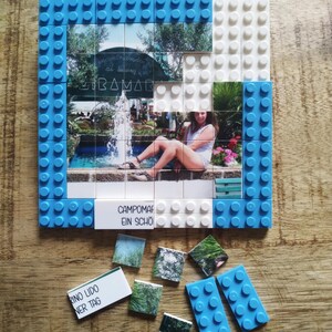 May include: A square building block mosaic featuring a photograph of a person sitting by a fountain. The frame is constructed from blue and white plastic bricks. Some blocks are loose, including pieces with the text CAMPOMARINO LIDO EIN SCH&Ouml;NER TAG.