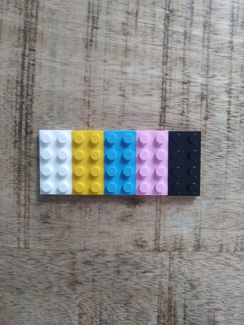 May include: A row of five rectangular plastic building bricks, each featuring eight circular studs on the top surface. The bricks are arranged side-by-side in a sequence of white, yellow, bright blue, light pink, and black colors.