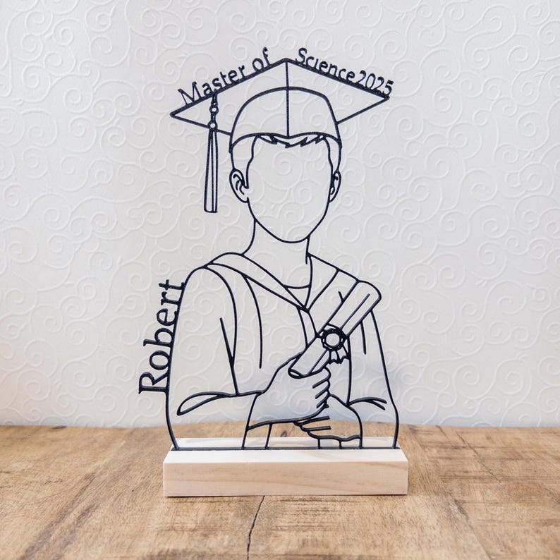 May include: A black line art graduation figure with a mortarboard hat and diploma, mounted on a wooden base. The text "Master of Science 2025" is above the figure's head, and the name "Robert" is on the side.