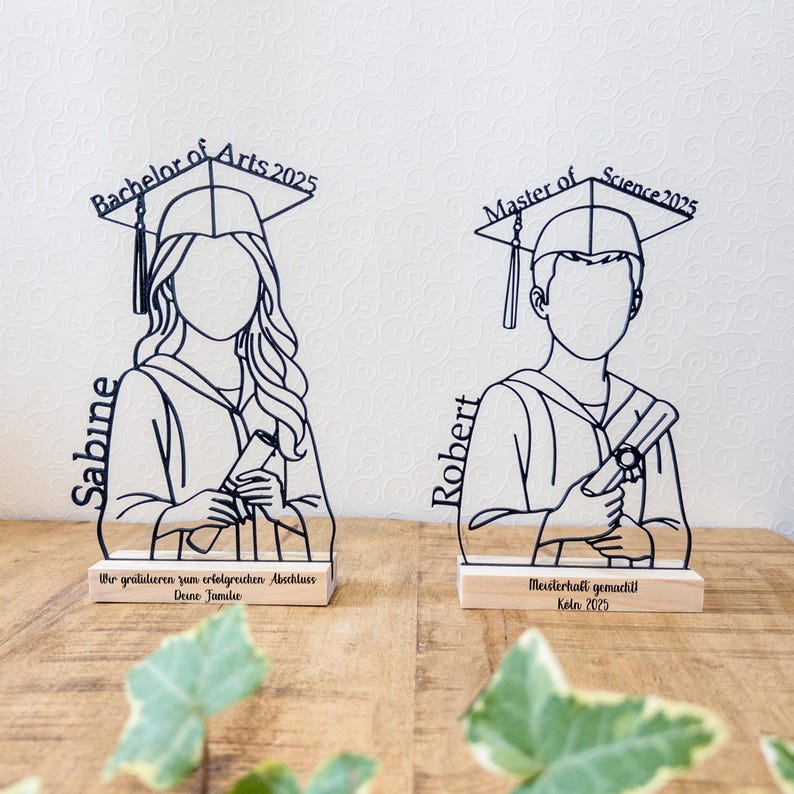 May include: Two graduation-themed wooden figurines. One is labeled "Bachelor of Arts 2025" and the other "Master of Science 2025". Each figure is a silhouette of a graduate holding a diploma. The base of each figure has text.