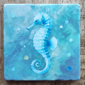 Puede incluir: Un caballito de mar azul y blanco pintado sobre un fondo azul y verde con puntos blancos. El caballito de mar está mirando hacia el lado derecho de la imagen.